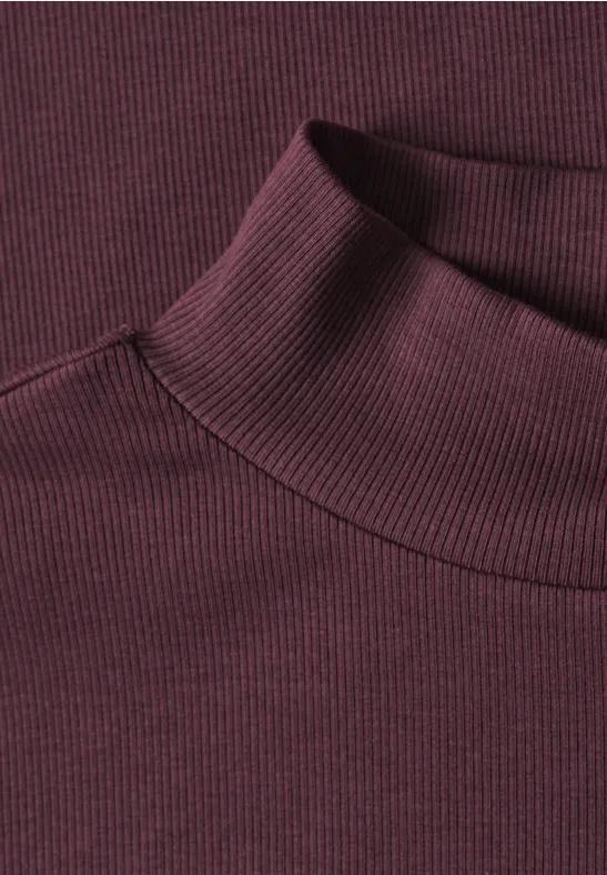 Detailaufnahme eines burgunderroten, fein gerippten Rollkragen-Pullovers.
