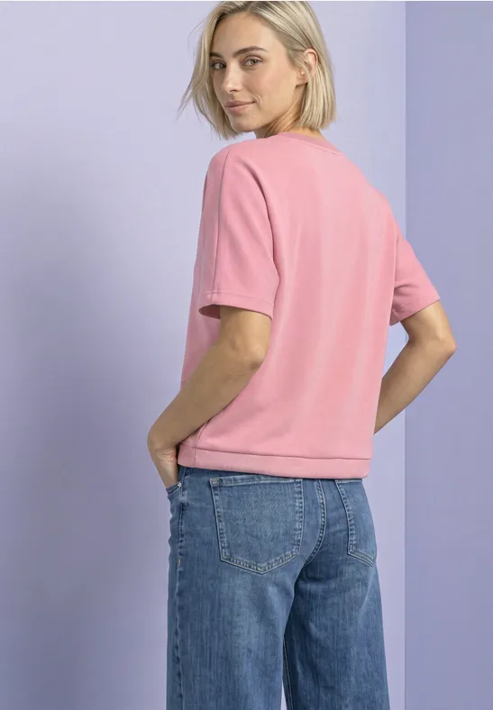 Jeune femme portant un T-shirt rose et un jean bleu, vue de côté.