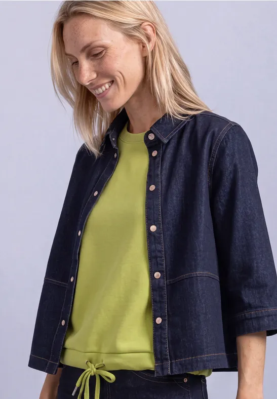 Blonde Frau in Jeansjacke und grünem Shirt, lächelnd, seitlicher Blick