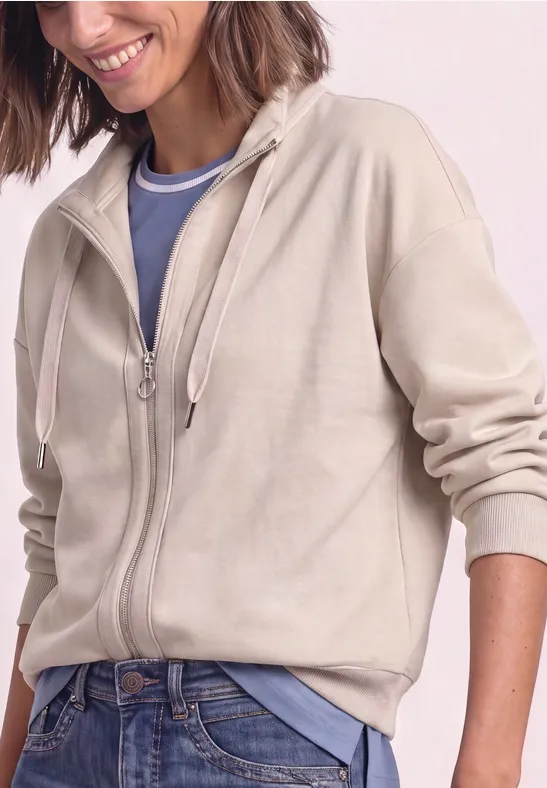 Frau trägt beigen Zip-Hoodie über blauem Shirt und Jeans.