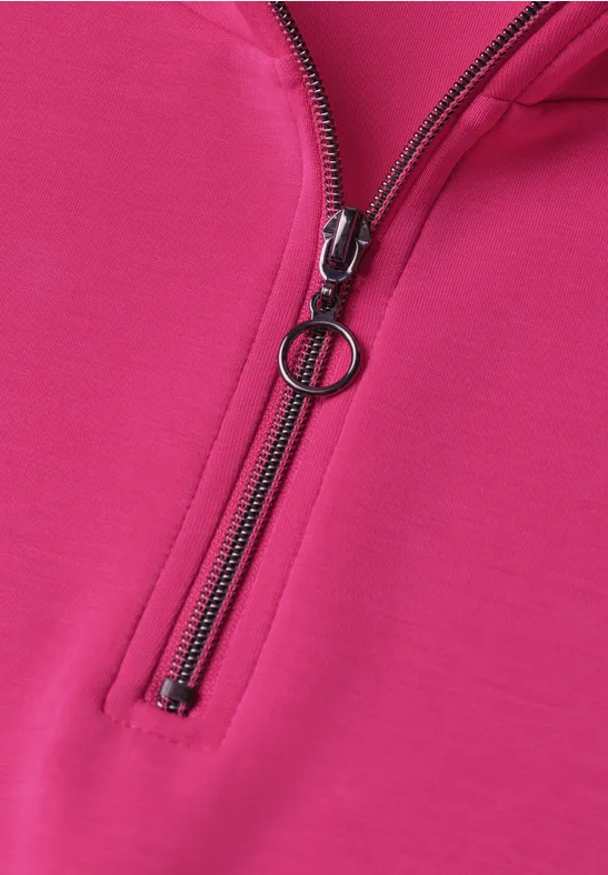 Nahaufnahme eines pinken Pullis mit schwarzem Reißverschluss und rundem Zipper-Anhänger.