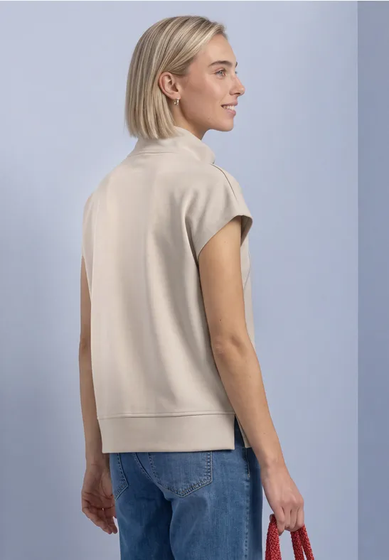 Frau mit kurzem blonden Haar trägt Beigetop und Jeans, seitlich im Bild, hält roten Beutel.