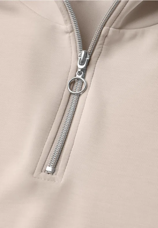 Beiger Kapuzenpullover mit halbem Reißverschluss und rundem Zipper-Anhänger.