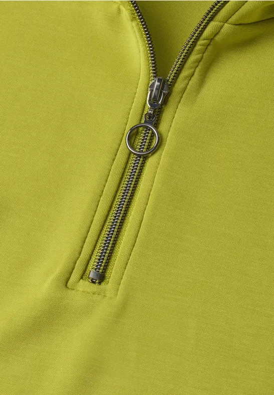 Nahansicht eines hellgrünen Oberteils mit Reißverschluss und rundem Zipper-Anhänger.
