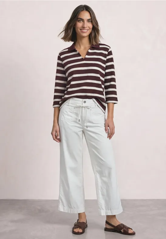 Frau trägt gestreiftes Oberteil und weiße, weite Jeans in neutralem Studio