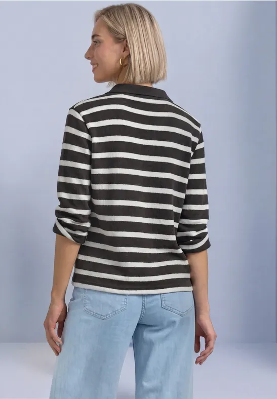 Frau von hinten in schwarz-weiß gestreiftem Shirt und hellblauen Jeans vor hellem Hintergrund.