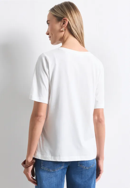 Eine Frau steht mit dem Rücken zur Kamera, trägt ein weißes T-Shirt und blaue Jeans.
