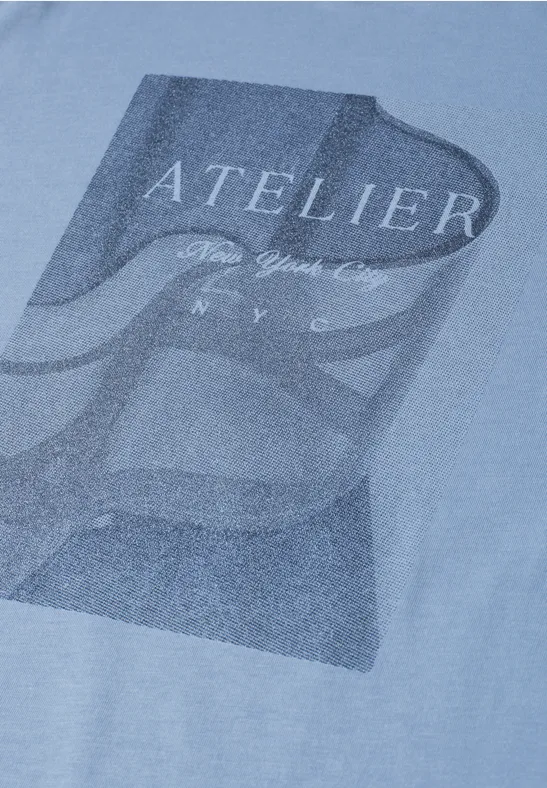 Hellblaues T-Shirt mit dunkelblauem Schriftzug 'ATELIER' und abstraktem Muster.