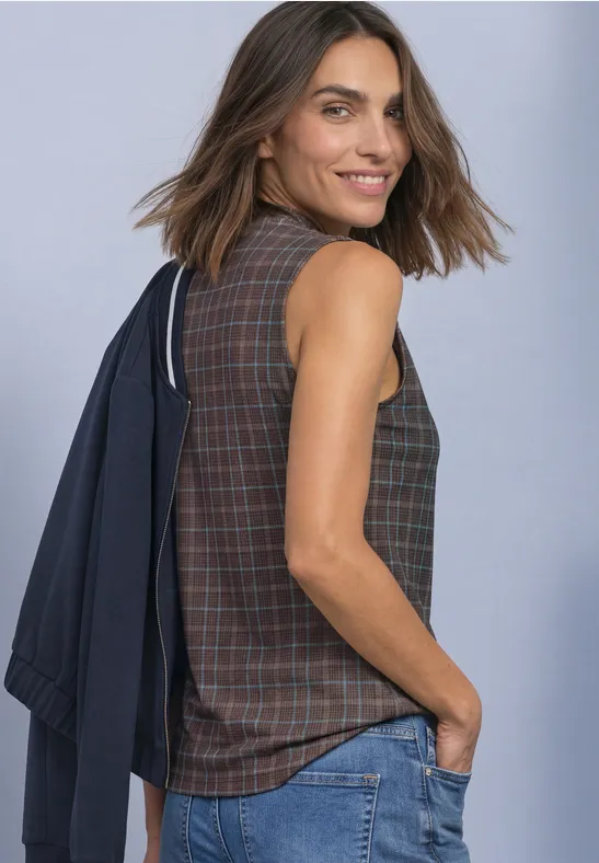 Frau mit schulterfreiem Blazer, karierte Bluse und Jeans, lächelt seitlich.