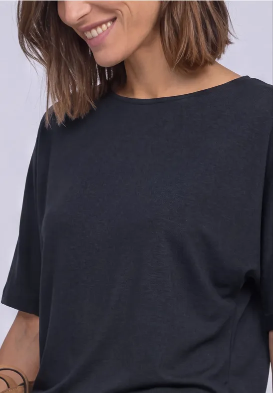 Eine lächelnde Frau mit schulterlangen braunen Haaren trägt ein schlichtes schwarzes T-Shirt.