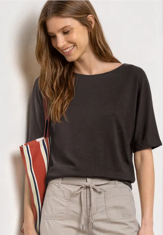 Vrouw in zwart T-shirt en beige trekkoordenbroek, draagt een gestreepte tas nonchalant aan de arm.