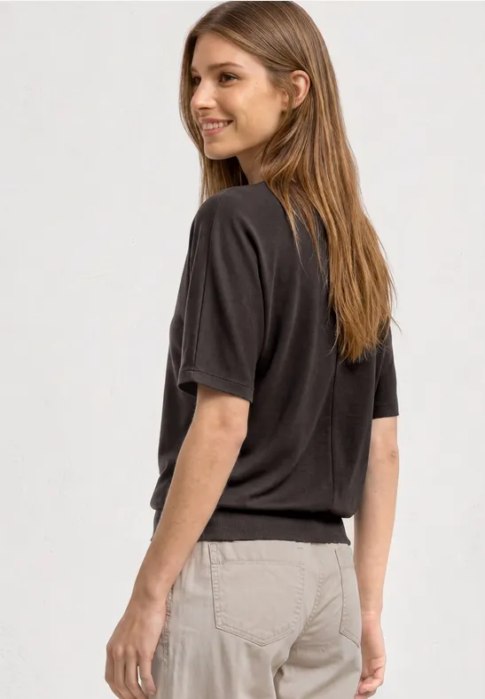 Zijaanzicht van een persoon met een donkergrijs t-shirt en lichte broek voor een witte achtergrond