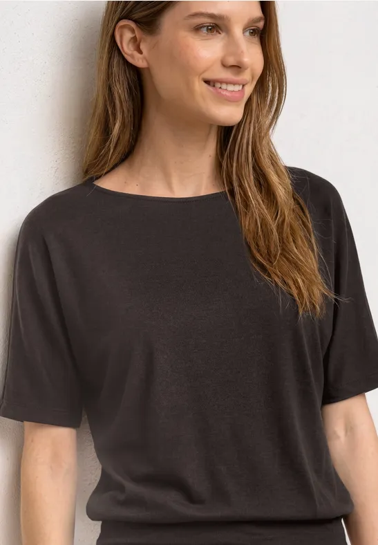 Vrouw met halflang bruin haar draagt een eenvoudig zwart t-shirt tegen een lichte achtergrond.