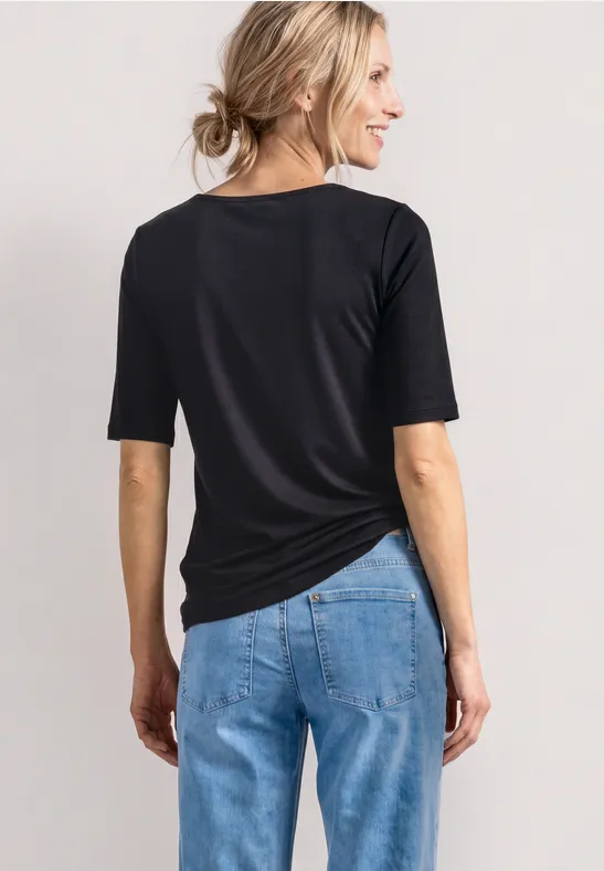 Vue de dos d'une femme en t-shirt noir et jean bleu sur fond clair.