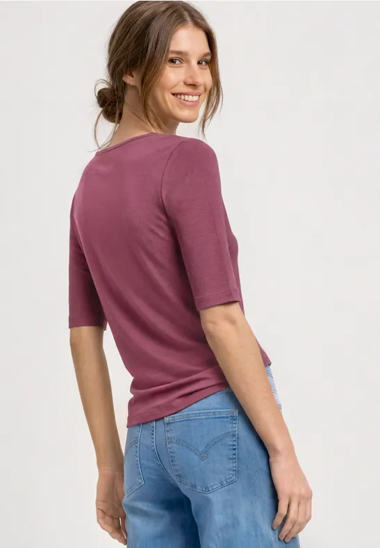 Femme de dos portant un haut violet et un jean bleu, fond clair.
