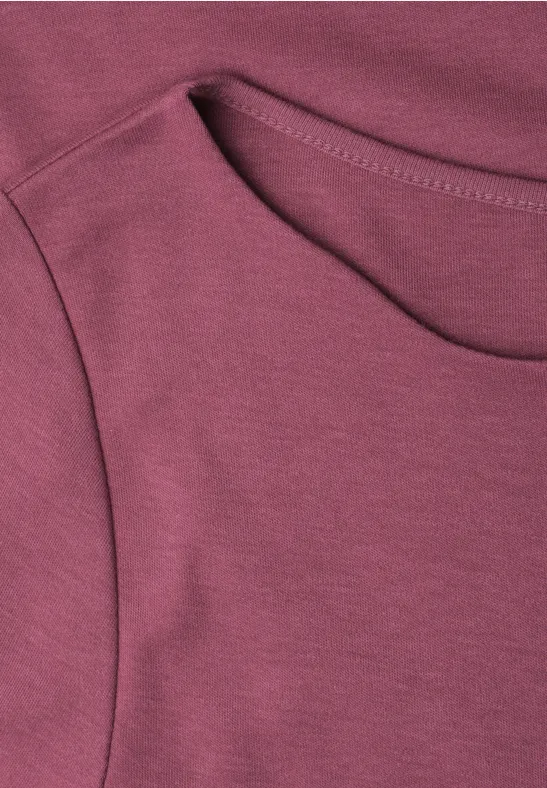 La photo montre un T-shirt bordeaux en gros plan, col rond et couture apparente.