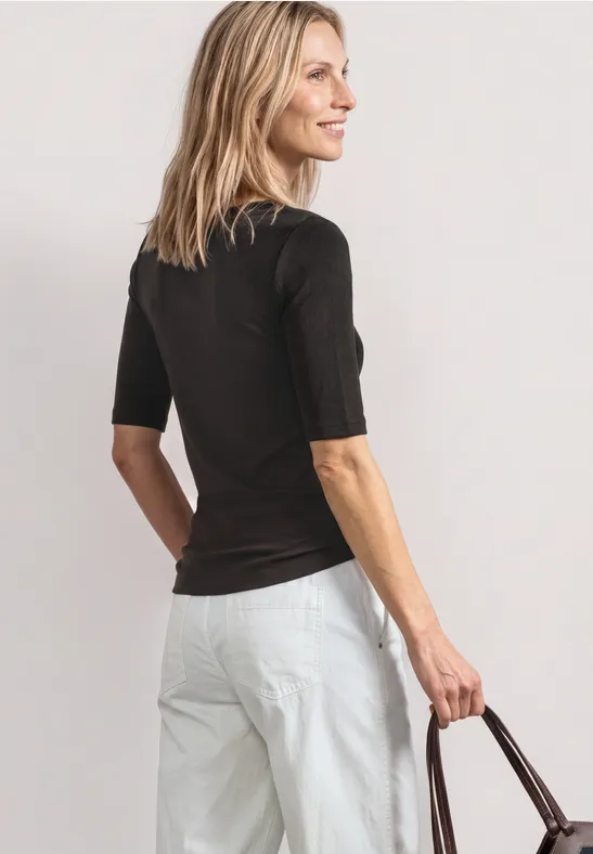 Femme de dos en haut noir et pantalon blanc, tenant un sac marron.