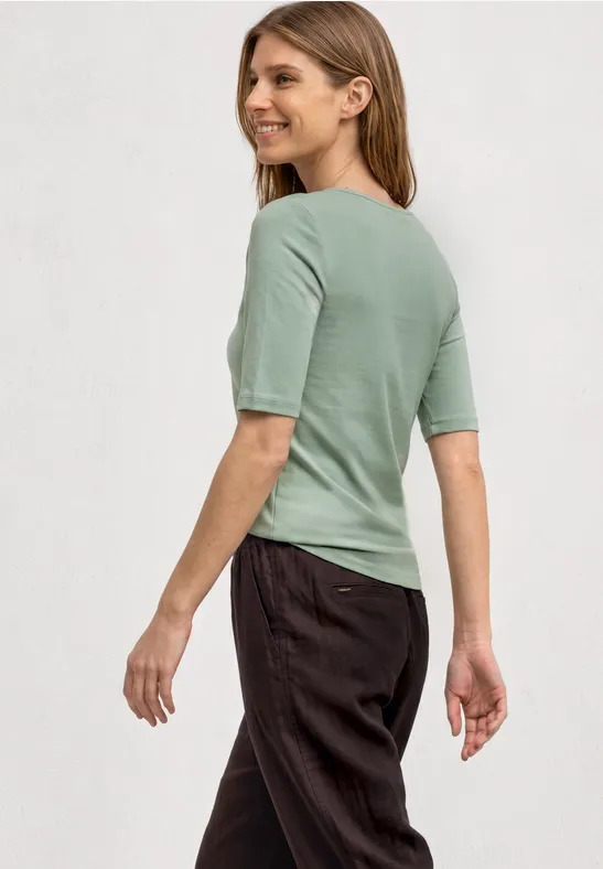 Eine Frau von hinten in einem pastellgrünen Kurzarmshirt und dunklen Hosen.