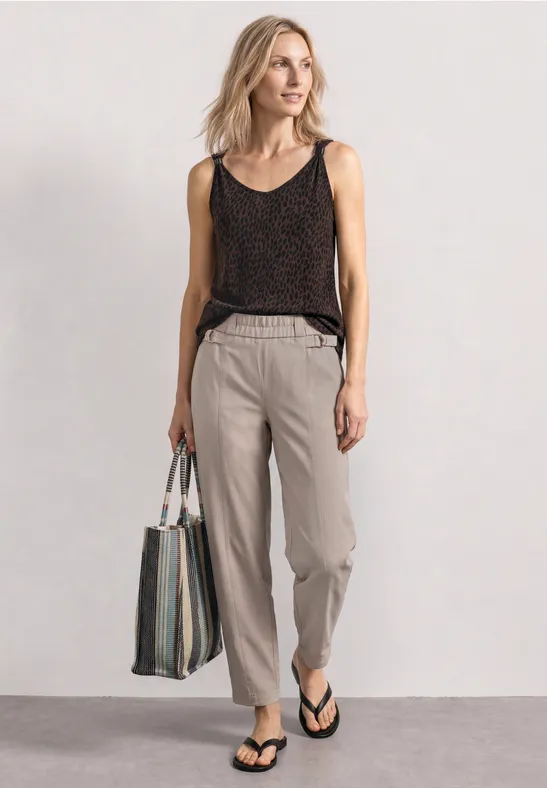 Frau trägt schwarzes Top, helle Hose, Flip-Flops und Tasche, lässiger Sommerlook.