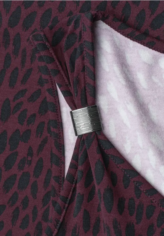 Ein dunkelroter Vorhang mit schwarzem Tupfenmuster, von einer silbernen Klammer zu eleganter Schleife gebunden.