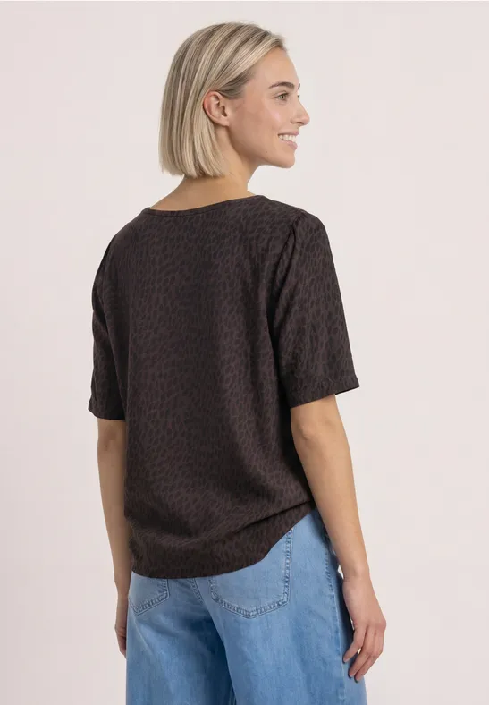 Frau von hinten mit kurzem, gemustertem T-Shirt in Dunkelbraun und hellblauen Jeans.