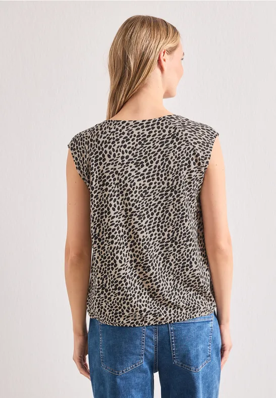 Frau von hinten in ärmellosem, gepunktetem Top und blauen Jeans vor hellem Hintergrund.