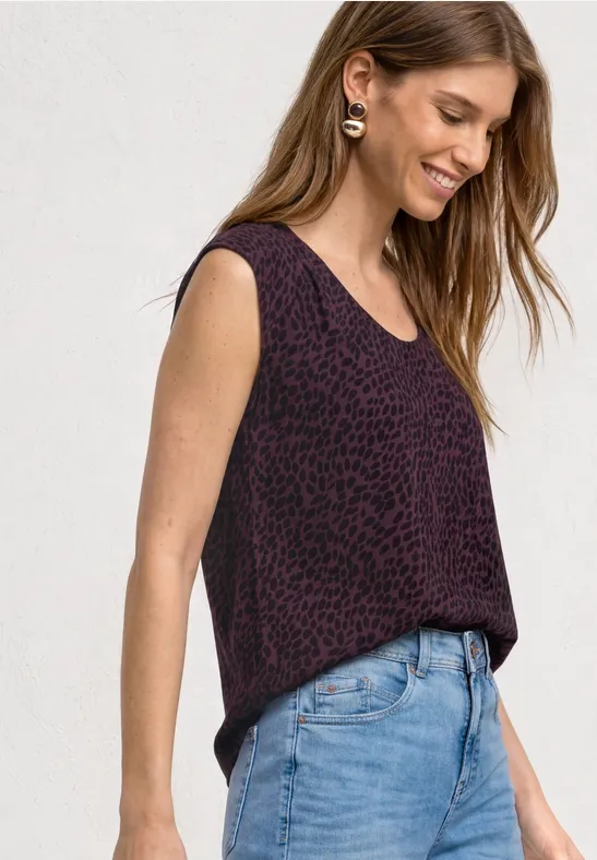 Frau in ärmellosem, violettem, gemustertem Top und hellblauen Jeans