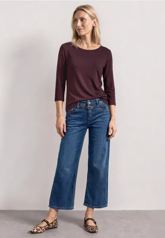 Frau mit langärmligem bordeauxfarbenem Shirt, weiten cropped Jeans und Leopardenmuster-Sandalen.