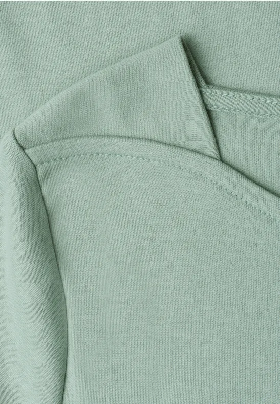 Nahaufnahme eines mintgrünen Baumwollshirts mit überlappendem Rundhalsausschnitt und Ziernaht.