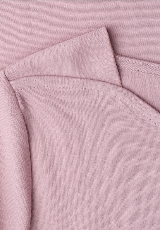 Nahaufnahme von rosa Baumwollstoff mit sichtbaren Nähten, vermutlich Teil eines T-Shirts oder Babykleidung.