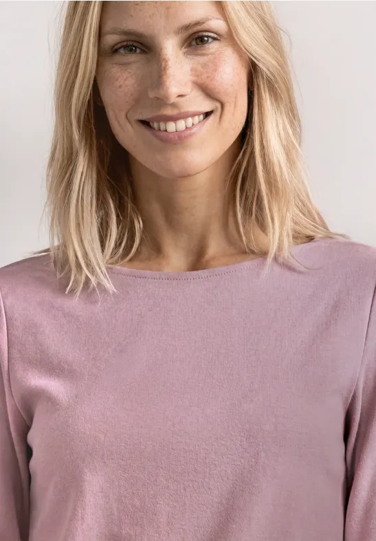 Eine Frau mit blonden Haaren und unscharfem Gesicht trägt ein rosafarbenes Oberteil.