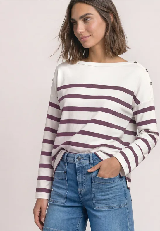Frau trägt weiß-lila gestreiftes Langarmshirt, blaue High-Waist-Jeans, eine Hand in der Tasche.