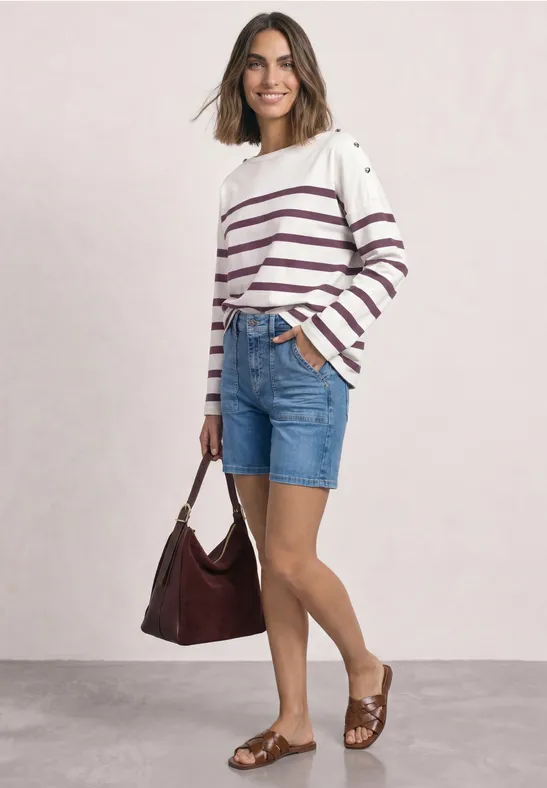 Frau in gestreiftem Pullover, Jeans-Shorts, braunen Sandalen mit passender Tasche vor hellem Hintergrund.