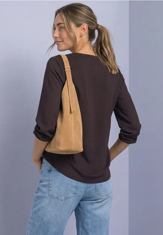 Frau mit Pferdeschwanz trägt schwarzen Pullover, helle Jeans und beigetone Wildledertasche über der Schulter.