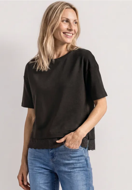 Uśmiechnięta kobieta w czarnym T-shircie i niebieskich dżinsach na jasnym tle.