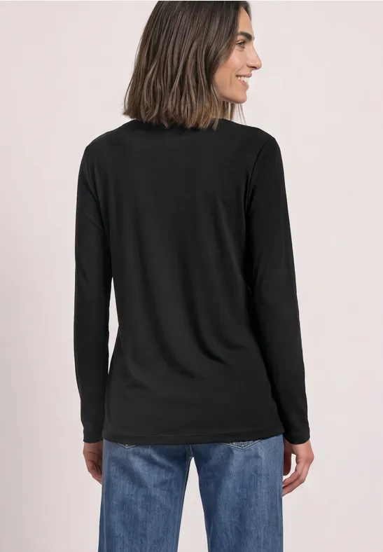 Frau von hinten in schwarzem Langarmshirt und blauen Jeans, schulterlanges Haar, lächelt seitlich