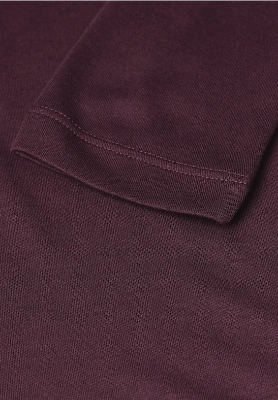 Close-up van een bordeauxrood kledingstuk met een zichtbare zoom en steeknaad.