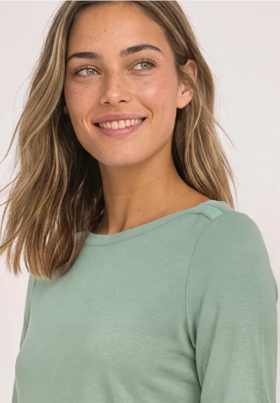 Frau mit langen braunen Haaren in grüner Bluse, die lächelnd in die Kamera blickt.