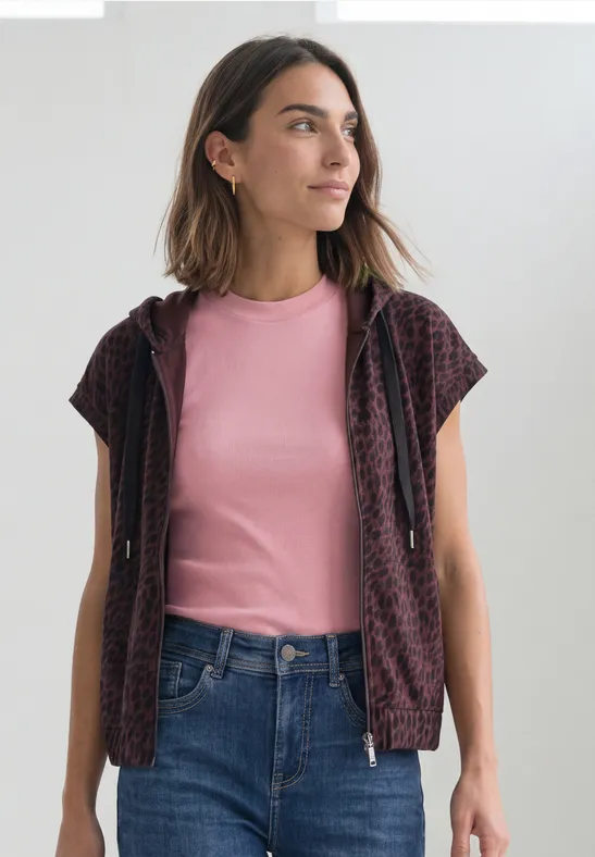 Frau in pinkem T-Shirt und gemustertem Cardigan, blickt seitlich.