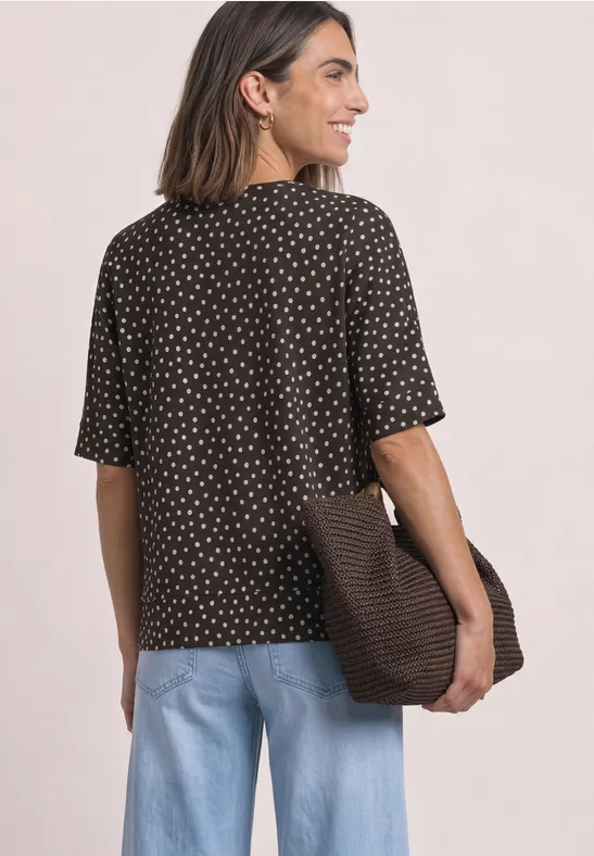Frau von hinten in braun gepunktetem Shirt, hellblauen Jeans, trägt eine große Tasche über der Schulter.