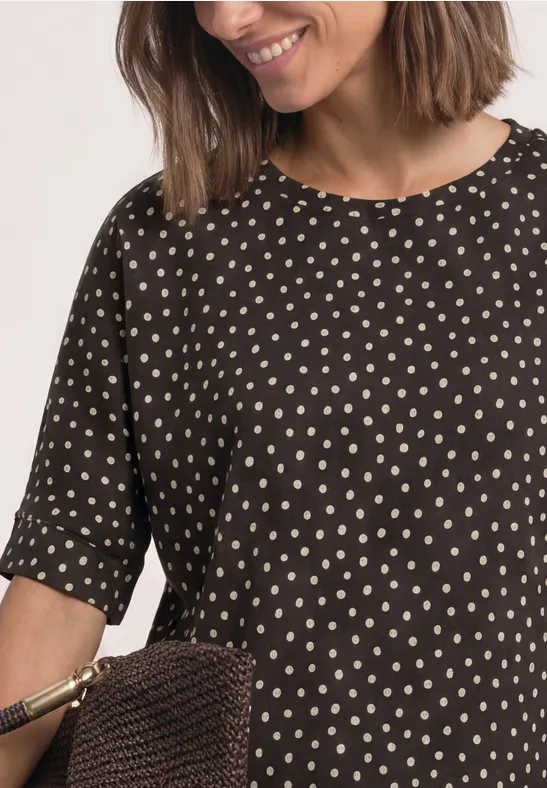 Frau trägt schwarze Bluse mit weißen Punkten und hält eine braune gewebte Tasche.