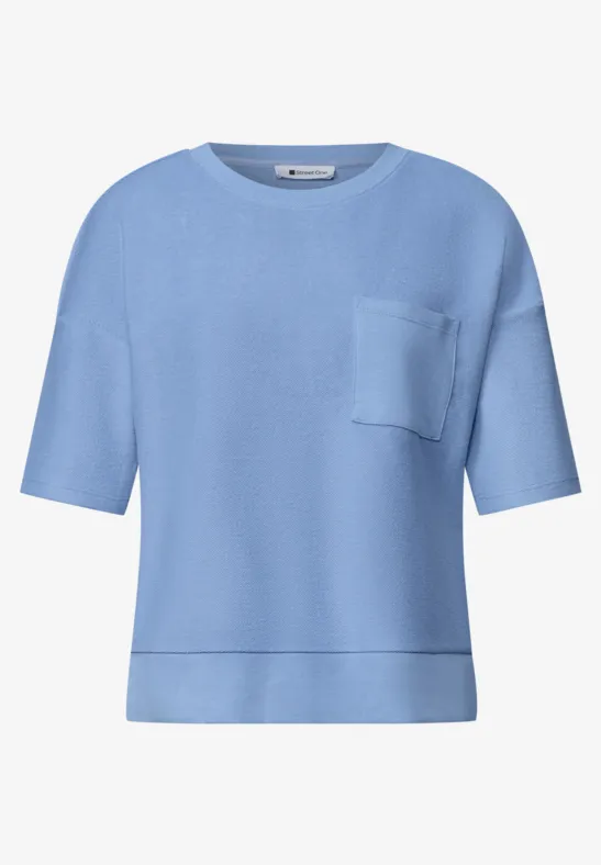 Lichtblauw T-shirt met korte mouwen, ronde hals, borstzakje en losse pasvorm.