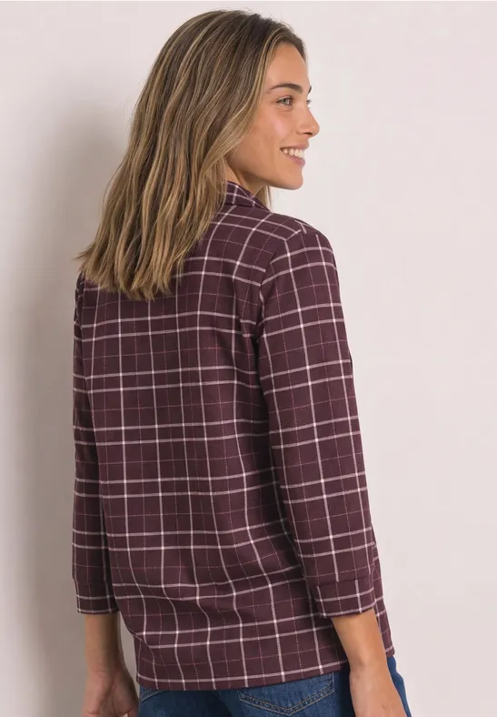 Frau seitlich mit bordeauxrotem kariertem Hemd (3/4-Ärmel) und heller Jeans.