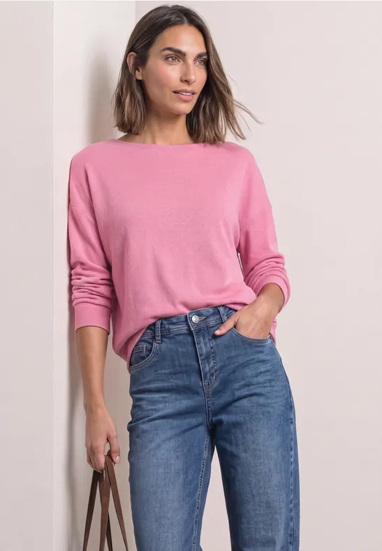 Vrouw in roze trui en blauwe jeans met een tas.