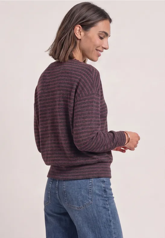 Frau mit gestreiftem Pullover und Jeans, seitlich stehend und lächelnd.