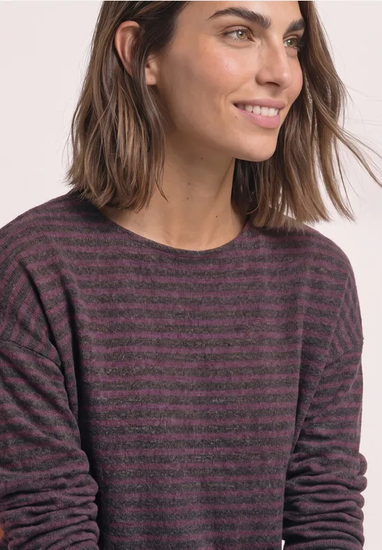 Eine Frau mit mittellangen Haaren trägt ein lila-schwarz gestreiftes Langarmshirt und lächelt leicht.