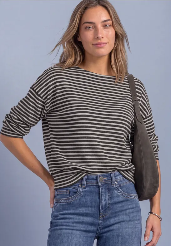 Frau im gestreiften Shirt und Jeans, lässig mit Umhängetasche posierend