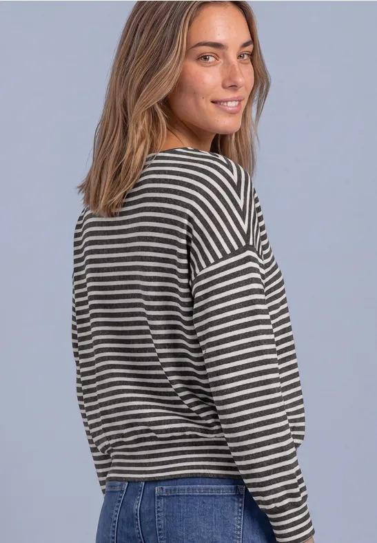Eine junge Frau mit hellbraunem Haar trägt gestreiftes Langarmshirt und Jeans, schaut lächelnd über die Schulter.