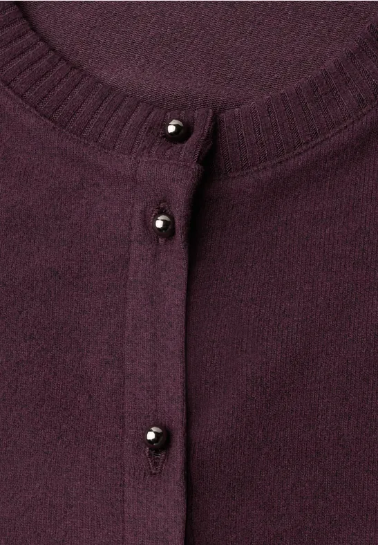 Gros plan sur un gilet violet à petits boutons noirs en perles.