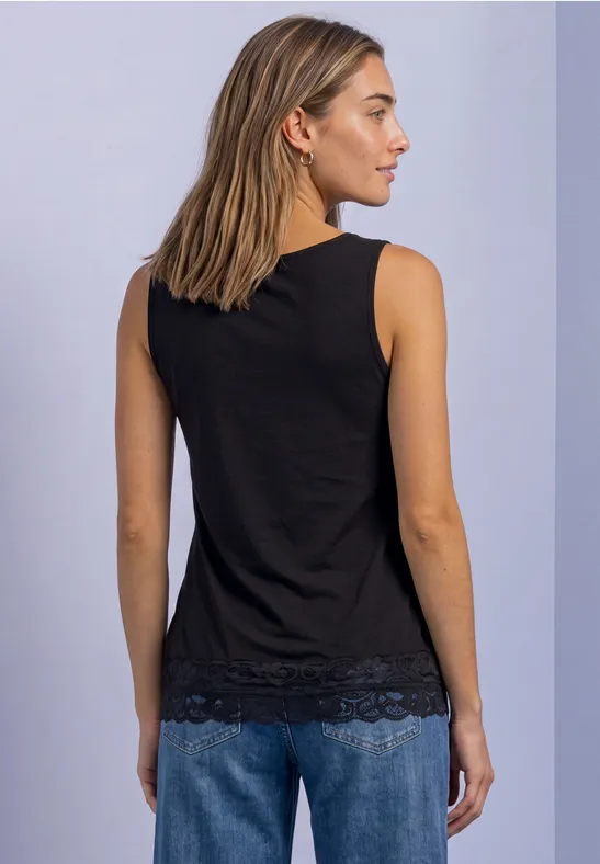 Rückansicht einer Frau in schwarzem ärmellosem Top mit Spitzensaum und blauen Jeans vor hellem Hintergrund.